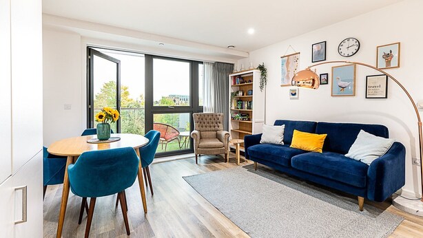 Un salon moderne avec un canapé bleu, une table à manger avec des chaises et une bibliothèque.