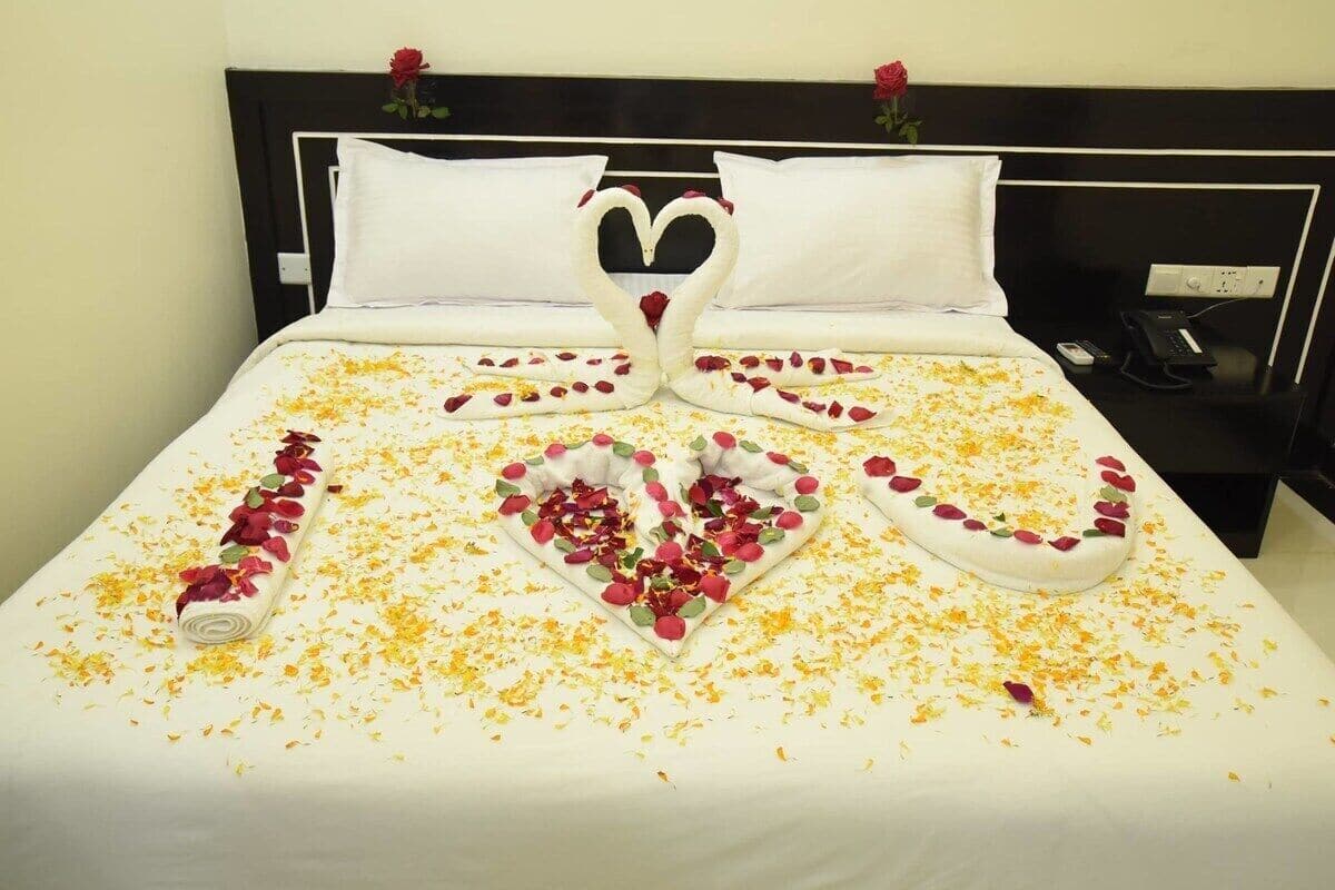 A bed with a heart-shaped arrangement of rose petals and a rolled towel.
