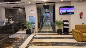 A hotel lobby with a reception desk, a TV mounted on the wall, a fire extinguisher, and a yellow sofa. - Elaf International Cox's Bazar (Cox's Bazar)