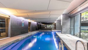 Une piscine intérieure offrant une vue dégagée sur l’espace piscine, avec des murs carrelés et une entrée par une porte vitrée.