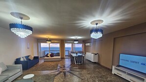 A modern living room with a large TV, two chandeliers, a dining area, and a view of the ocean. - Midpoint sea view - families only (Alexandria)