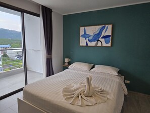 Une chambre avec un lit, un tableau et une vue sur un immeuble et de la verdure.