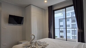A hotel room with a bed, a TV mounted on the wall, a wardrobe, and a window with curtains. - Sea Side Haven 1 Bed T2-621 (Chalong)
