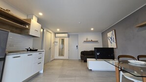 A modern kitchen with white cabinets, a dining area with a glass table, and a living space with a sofa and TV. - Sea Side Haven 1 Bed T2-621 (Chalong)