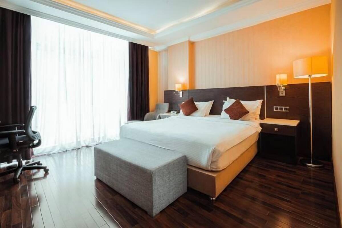 A hotel room with a large bed, a desk, a chair, a bedside table, and a lamp.