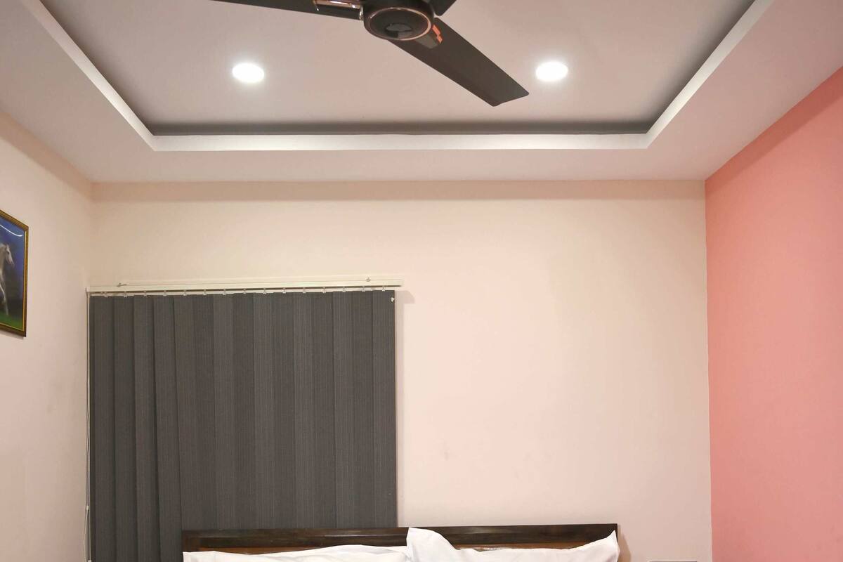 Une chambre à coucher avec un lit, un ventilateur de plafond, une fenêtre avec des stores et une table de chevet.