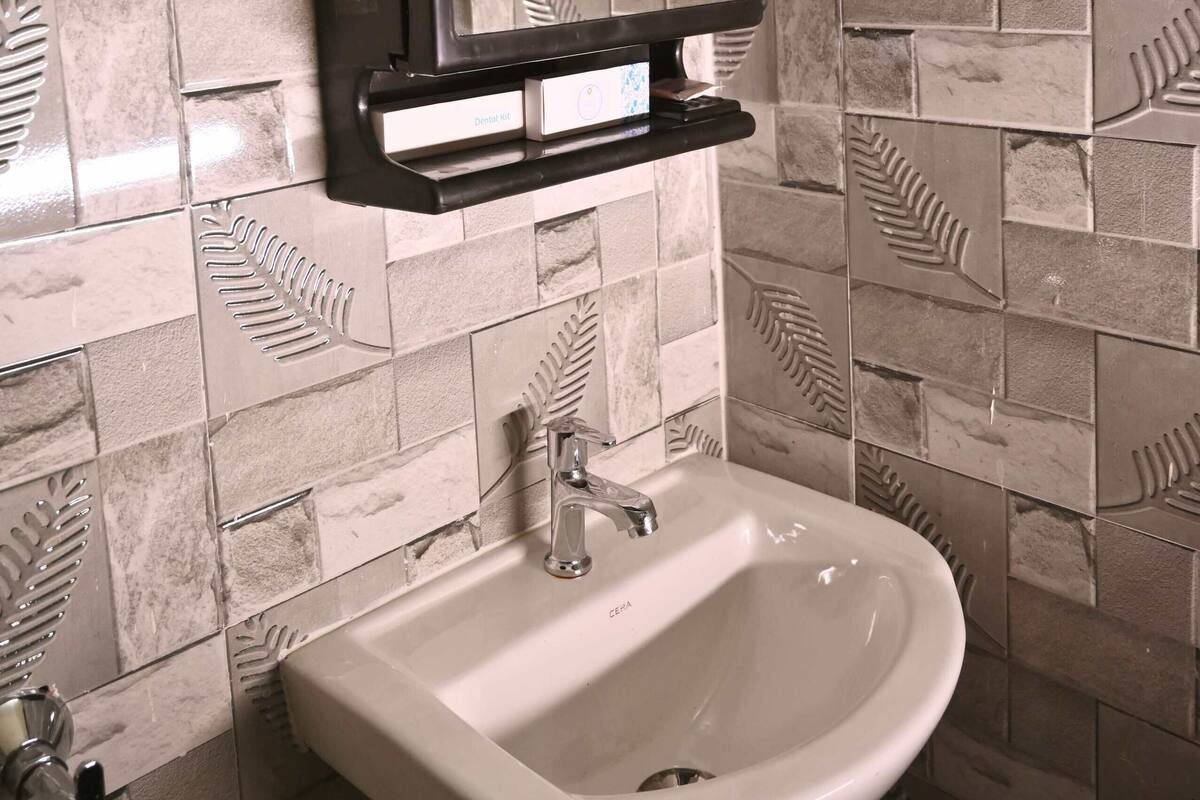Une salle de bain avec un lavabo blanc, un miroir et un mur orné d’un motif de feuilles.