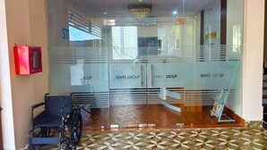 A reception area with a wheelchair, a red fire alarm box, and a patterned floor. - Stanza Premium Hotels (Bhubaneshwar)