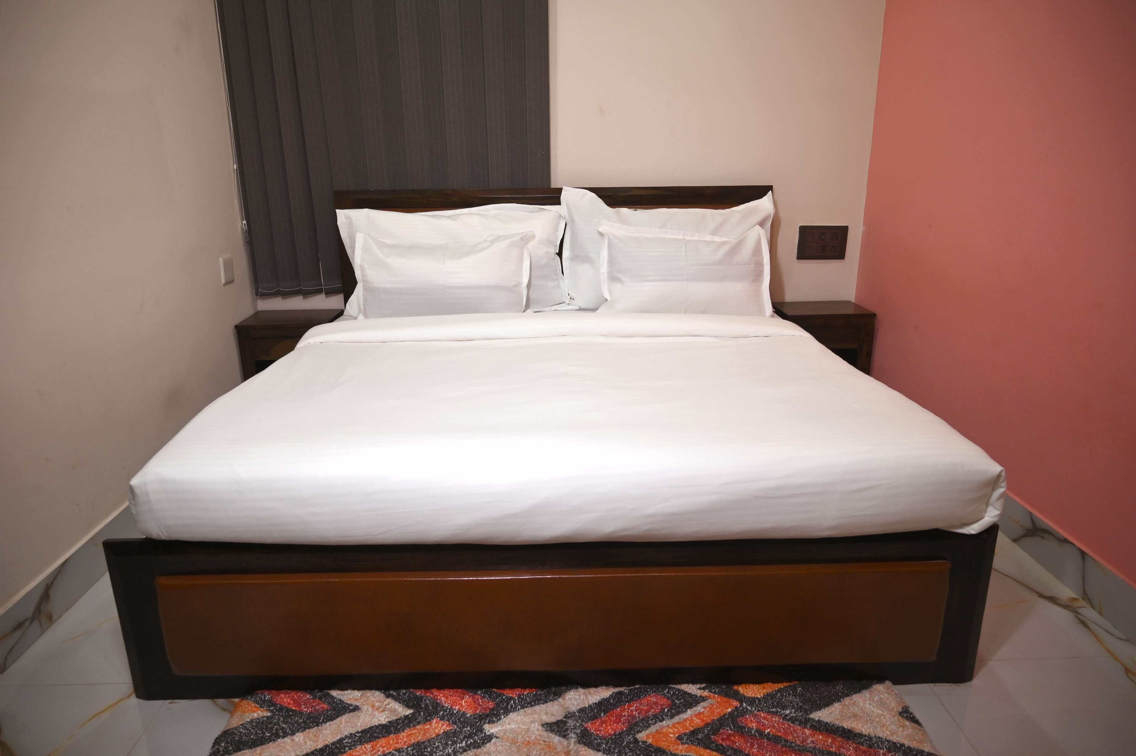 A neatly made bed with white linens and a wooden headboard in a room with a patterned rug.