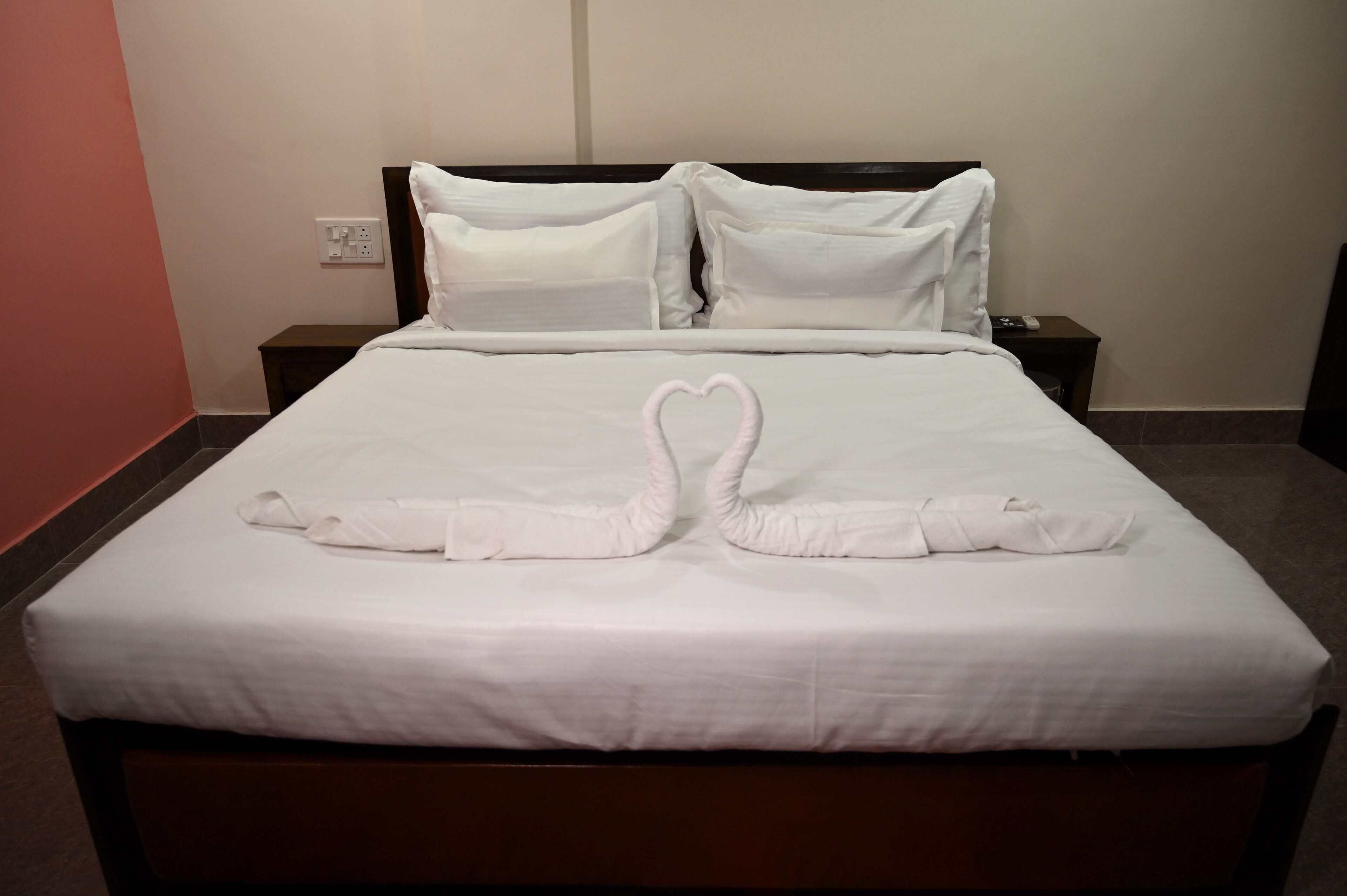 Un lit bien fait, avec du linge de lit blanc et une serviette pliée en forme de cœur posée sur le lit.
