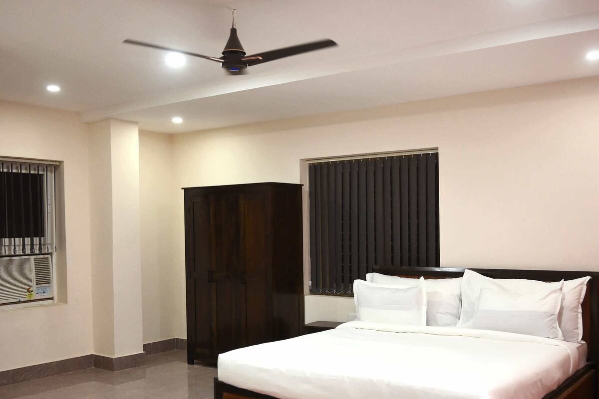 Une chambre à coucher avec un grand lit, un ventilateur de plafond, une armoire et une fenêtre avec des stores.