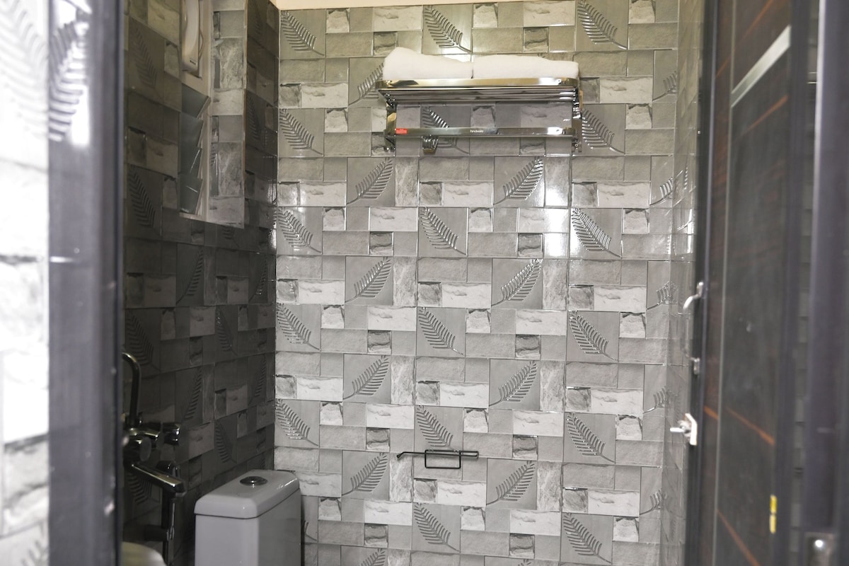 A compact bathroom with a toilet, a shower, and a trash bin.