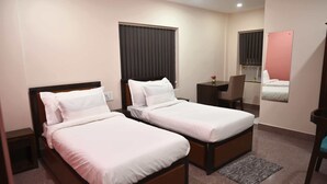 A hotel room with two single beds, a desk, a chair, a mirror, and a window with blinds. - Stanza Premium Hotels (Bhubaneshwar)