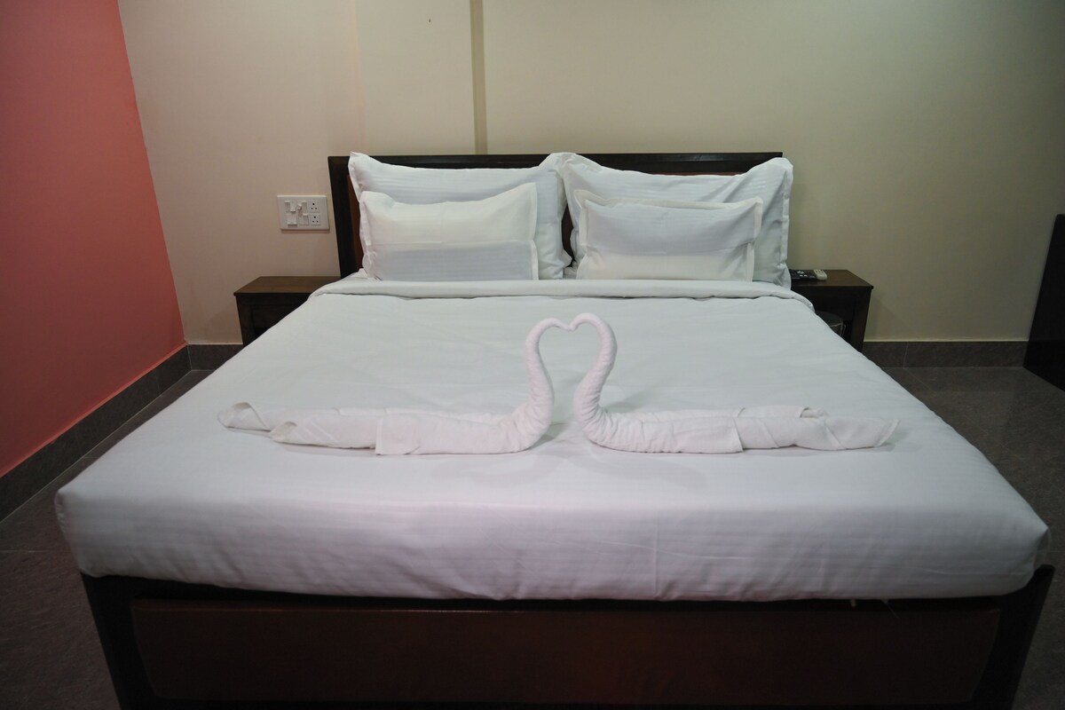 Een net opgemaakt bed met een handdoekje in de vorm van een hart, witte beddengoed en een houten hoofdbord.