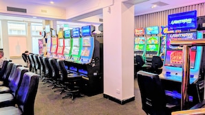 A row of slot machines with colorful displays, a seating area with chairs, and a television screen on the wall. - AMBASSADORS HOTEL ADELAIDE (Adelaide)