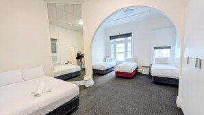 A hotel room with three beds, a large arched window, and a mirror reflecting the room. - AMBASSADORS HOTEL ADELAIDE (Adelaide)
