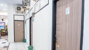 A hallway with tiled flooring, a green basket, and closed doors with a sign indicating room number 1F. - Tamastu House Pasar Baru Jakarta (Jakarta)