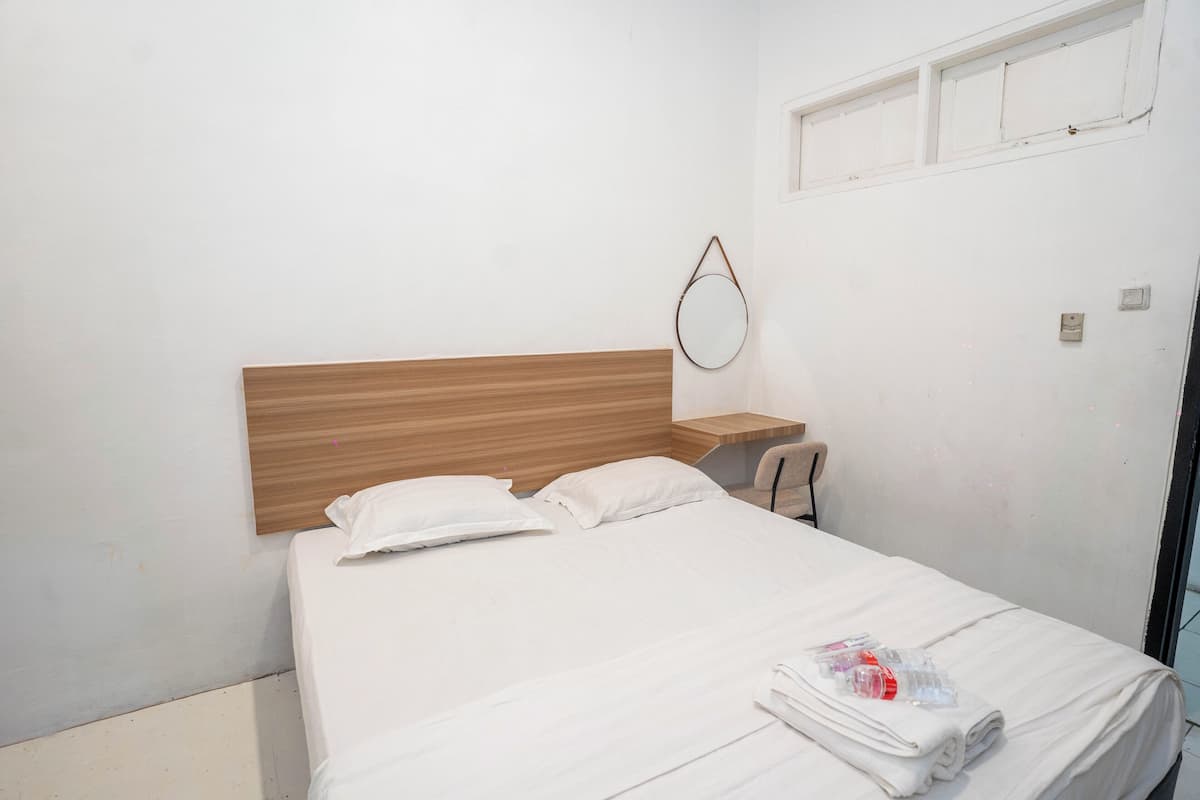 A neatly made bed with white linens, a wooden headboard, a small bedside table, and a round mirror on the wall.