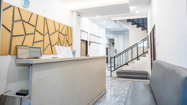 A reception area with a modern design, including a reception desk, a wall clock, and a staircase leading to an upper floor. - Tamastu House Pasar Baru Jakarta (Jakarta)