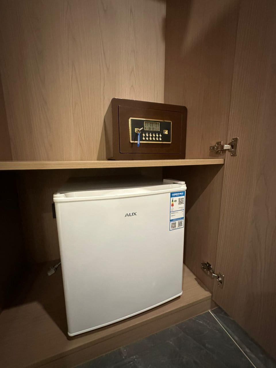 Ett litet, vitt kylskåp med ett digitalt lås och en kontrollpanel på ovansidan, placerat under ett träskåp.
