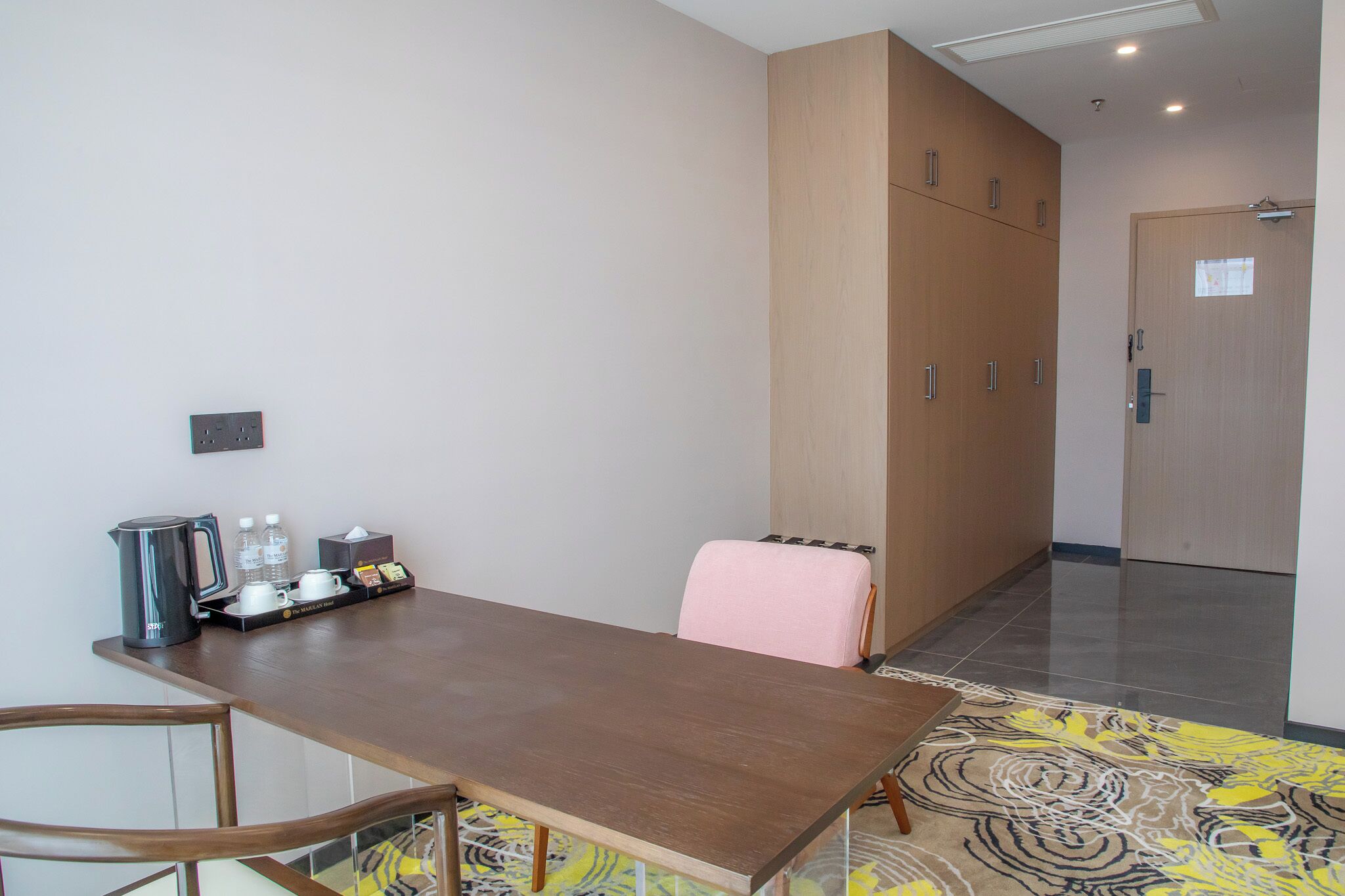 A hotel room with a wooden table, chairs, a radiator, and a door with a window.