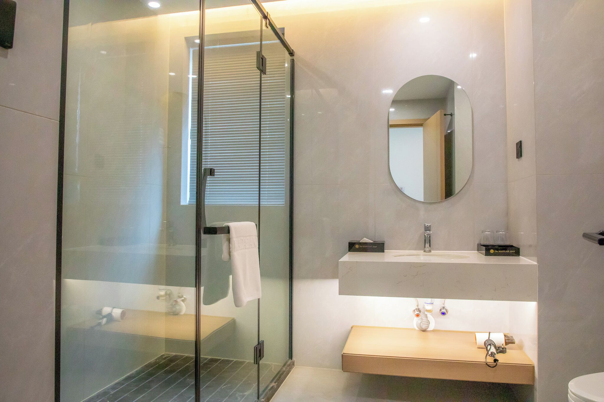 A modern bathroom with a glass-enclosed shower, a round mirror, and a wooden vanity with a sink.