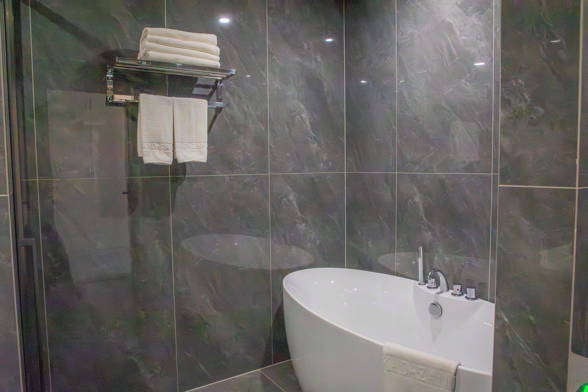 Un baño moderno con una bañera independiente, un perchero con toallas dobladas y baldosas de mármol oscuro.