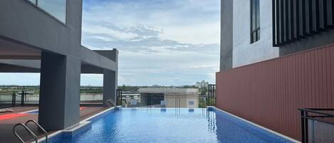 Una piscina en la azotea con agua cristalina y azul, rodeada de arquitectura moderna y vistas a edificios distantes.
