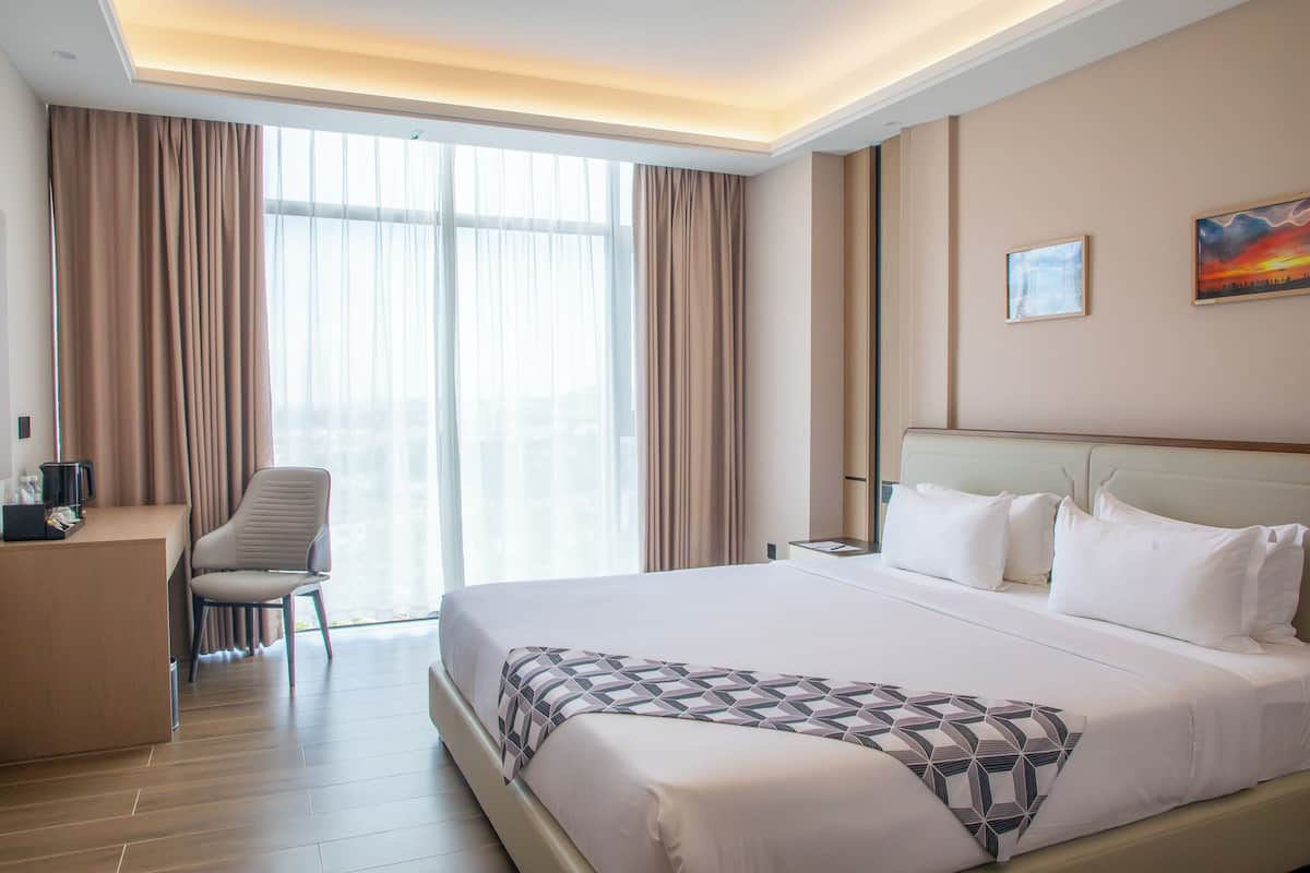 Ein Hotelzimmer mit einem großen Bett, einem Schreibtisch, einem Stuhl und einem Fenster mit Vorhängen.