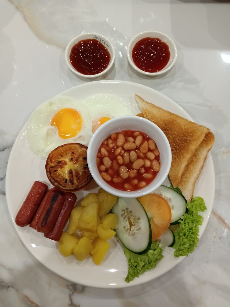 Un plato de comida para el desayuno con huevos, tostadas, frijoles, salchichas, piña, pepino y lechuga.