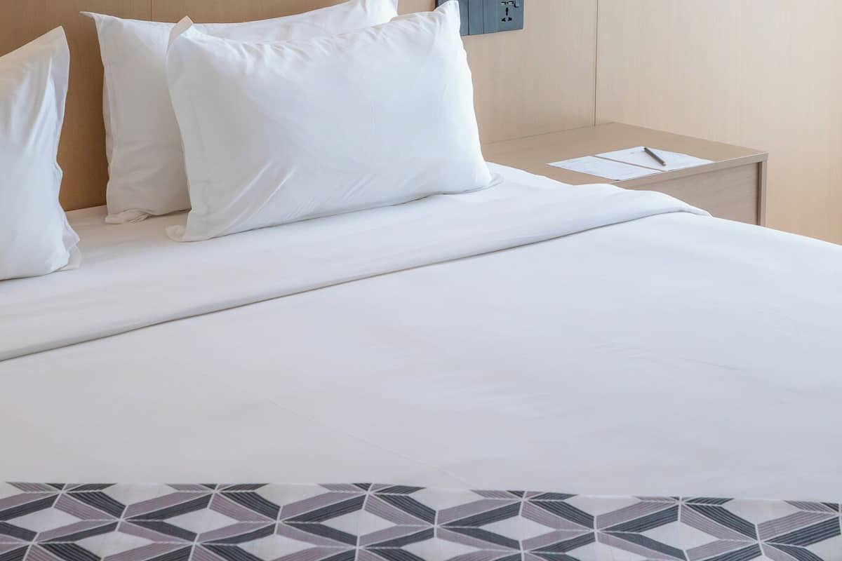 Ein Hotelzimmer mit Bett, Kissen, einem Nachttisch und einer Steckdose.