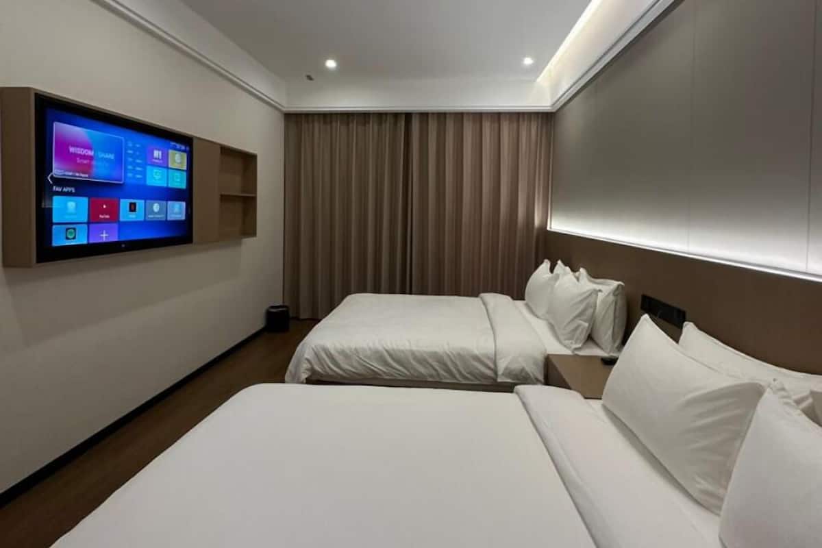 Ein Hotelzimmer mit zwei Betten, einem an der Wand montierten Flachbildfernseher und einer Decke mit Einbaustrahlern.