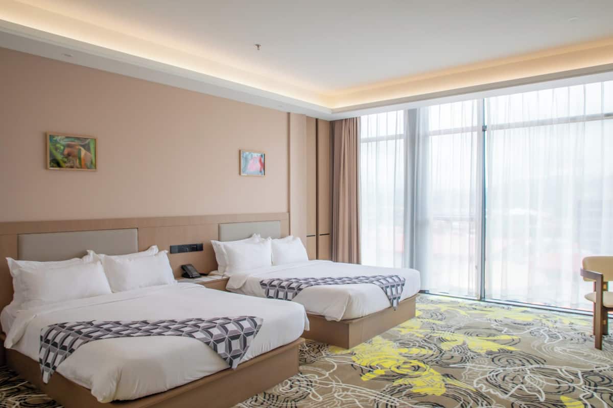 Ein Hotelzimmer mit zwei Betten, einem großen Fenster mit Vorhängen, einem Schreibtisch und einem Stuhl.