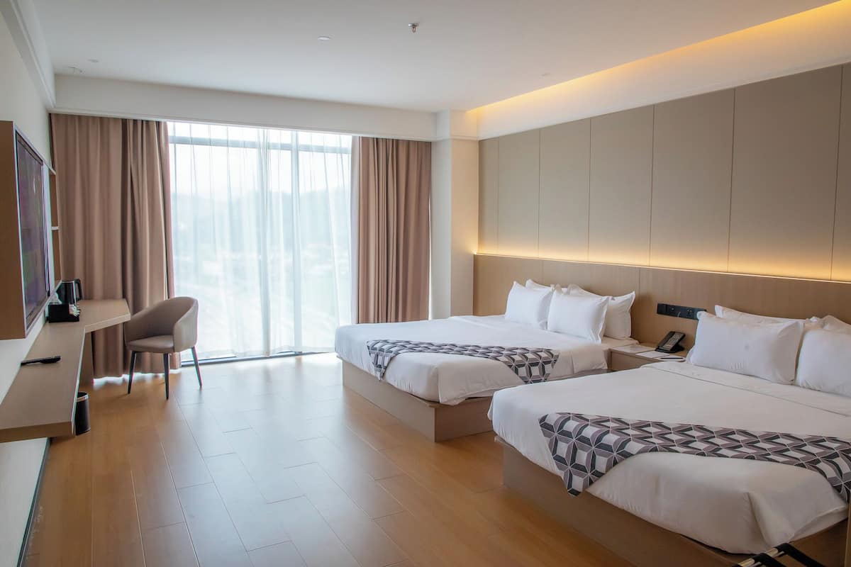 Ein Hotelzimmer mit zwei Betten, einem Schreibtisch, einem Sessel und einem großen Fenster mit Vorhängen.