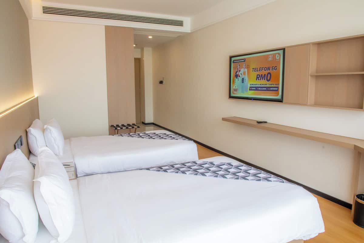 Ein Hotelzimmer mit zwei Betten, einem Wandfernseher und einem Regal.
