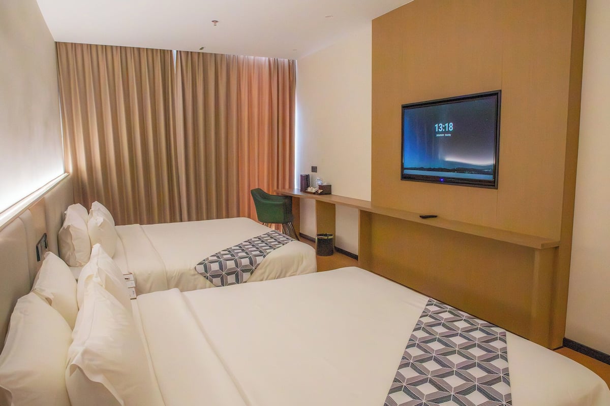 Ein Hotelzimmer mit zwei Betten, einem Schreibtisch, einem Sessel, einem Fernseher und einem großen Fenster mit Vorhängen.