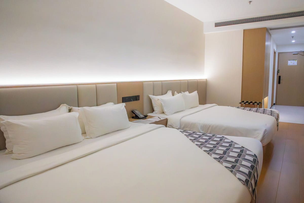 Ein Hotelzimmer mit zwei Betten, einem Nachttisch mit Telefon und einer Tür zu einem weiteren Raum.