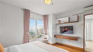 A modern hotel room with a large bed, a TV mounted on the wall, and a city view.
