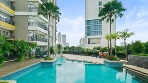 A swimming pool surrounded by modern buildings, palm trees, and a playground.