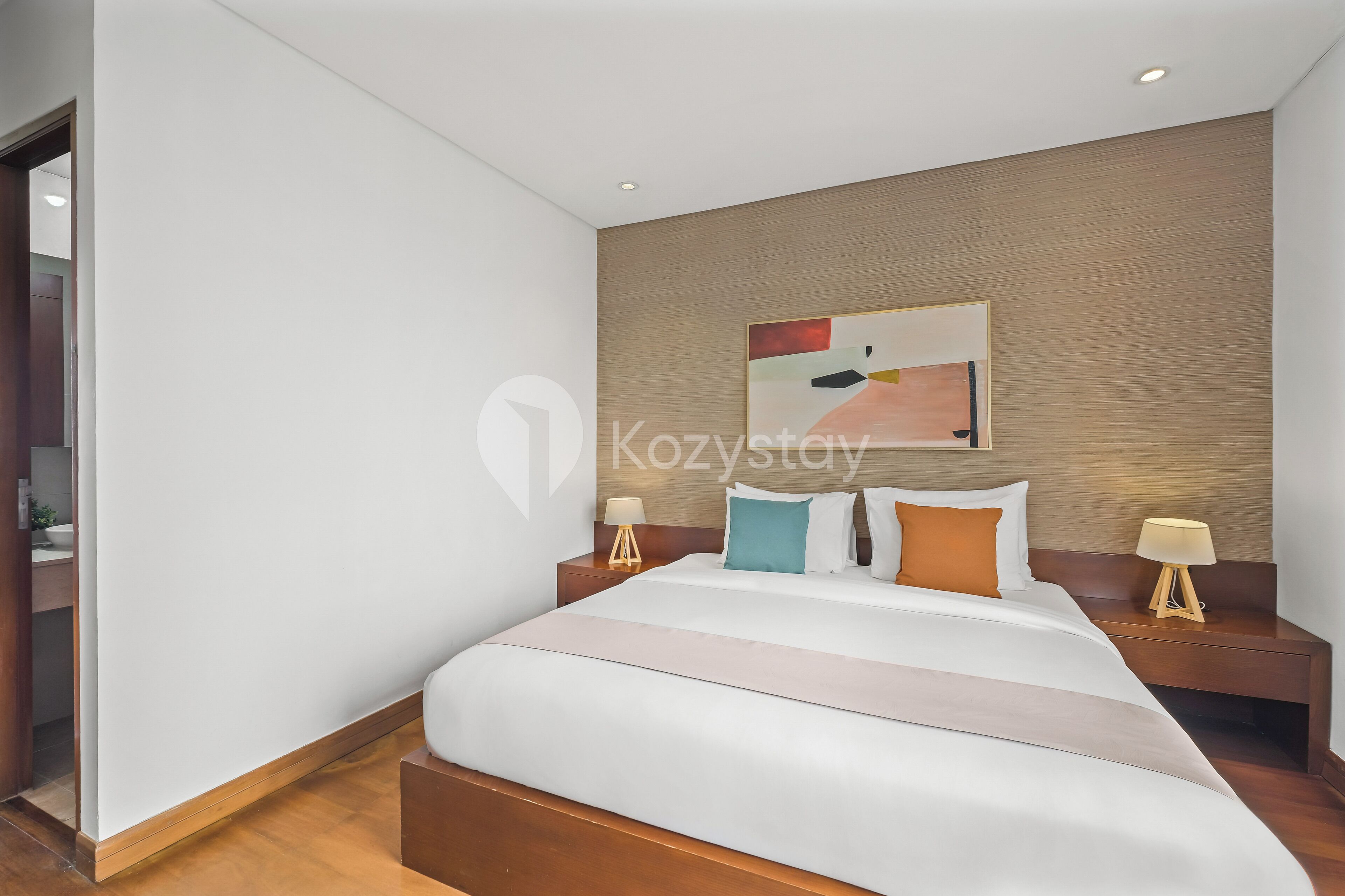 Una habitación de hotel moderna con una cama grande, dos mesitas de noche con lámparas, un cabecero de madera y un cuadro abstracto grande en la pared.