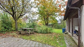 Une terrasse dallée avec une table de pique-nique, entourée d’arbres et d’une pelouse.