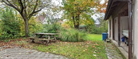 Ein gepflasterter Patio-Bereich mit Picknicktisch, umgeben von Bäumen und einer Rasenfläche.