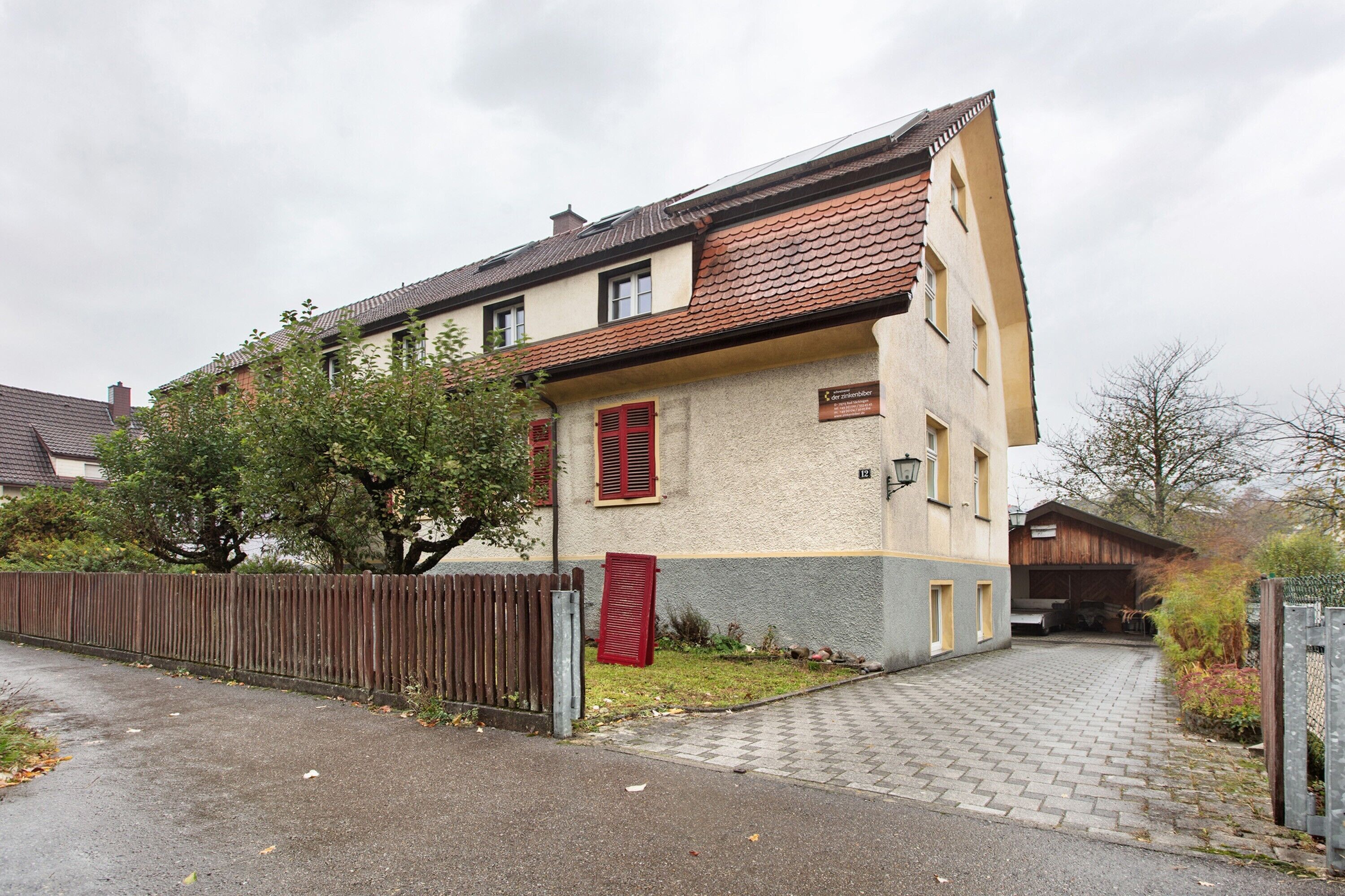 Un immeuble résidentiel de deux étages, doté d’une allée pavée et d’une clôture en bois.