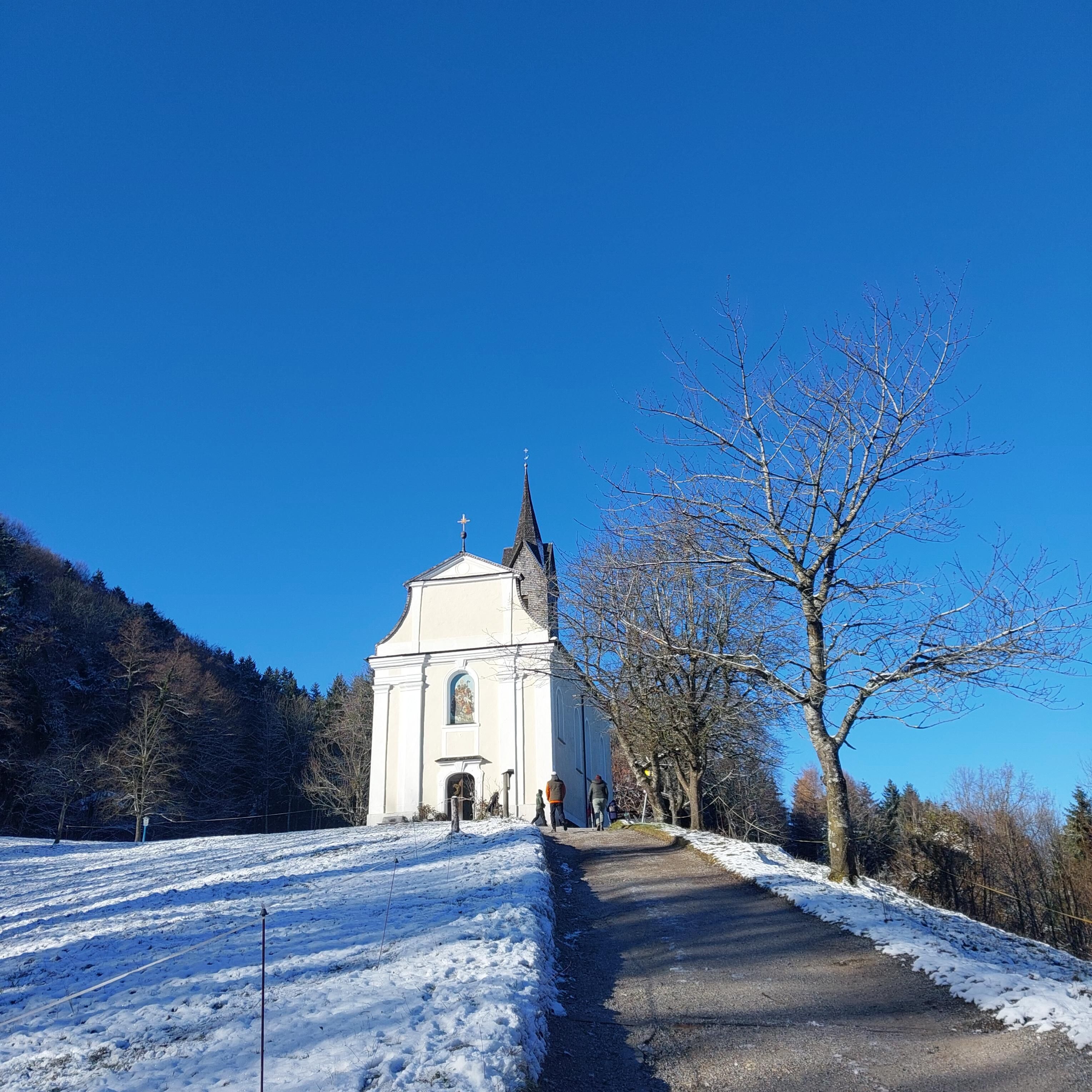 Una iglesia blanca con un campanario y un sendero cubierto de nieve que lleva a ella.