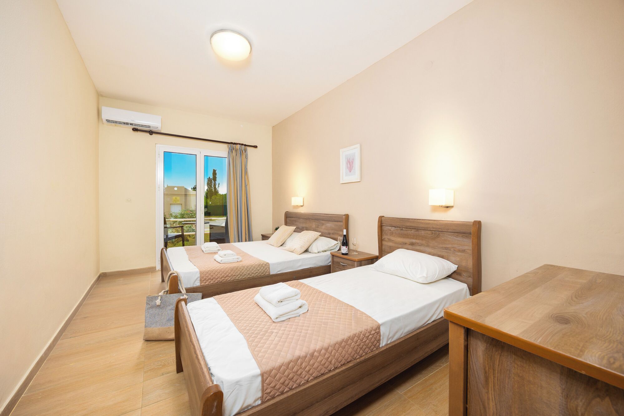 Une chambre d’hôtel avec deux lits simples, une table de chevet en bois, une petite table et une porte-fenêtre coulissante donnant sur un espace extérieur.