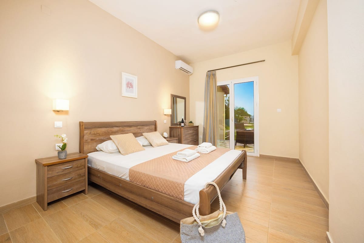 A hotel room with a wooden bed, a nightstand, a dresser, a mirror, and a sliding glass door to the balcony.