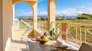A balcony with a table set for a meal, a bottle of wine, and a view of a mountainous landscape.