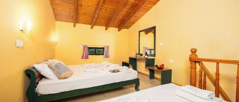 A room with a wooden ceiling, a bed with a green frame, a bedside table with a mirror, and a wooden staircase.
