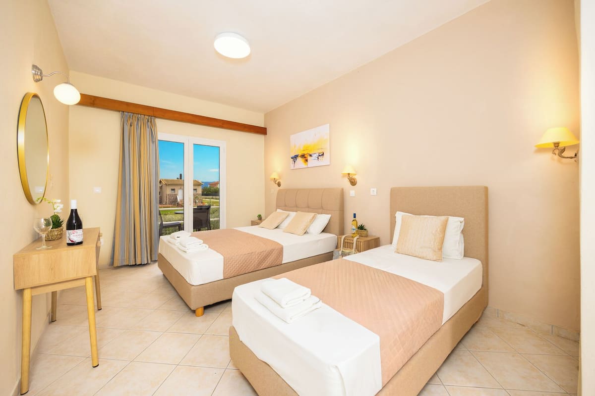 A hotel room with two beds, a wooden desk, a mirror, and a view of the outdoors.