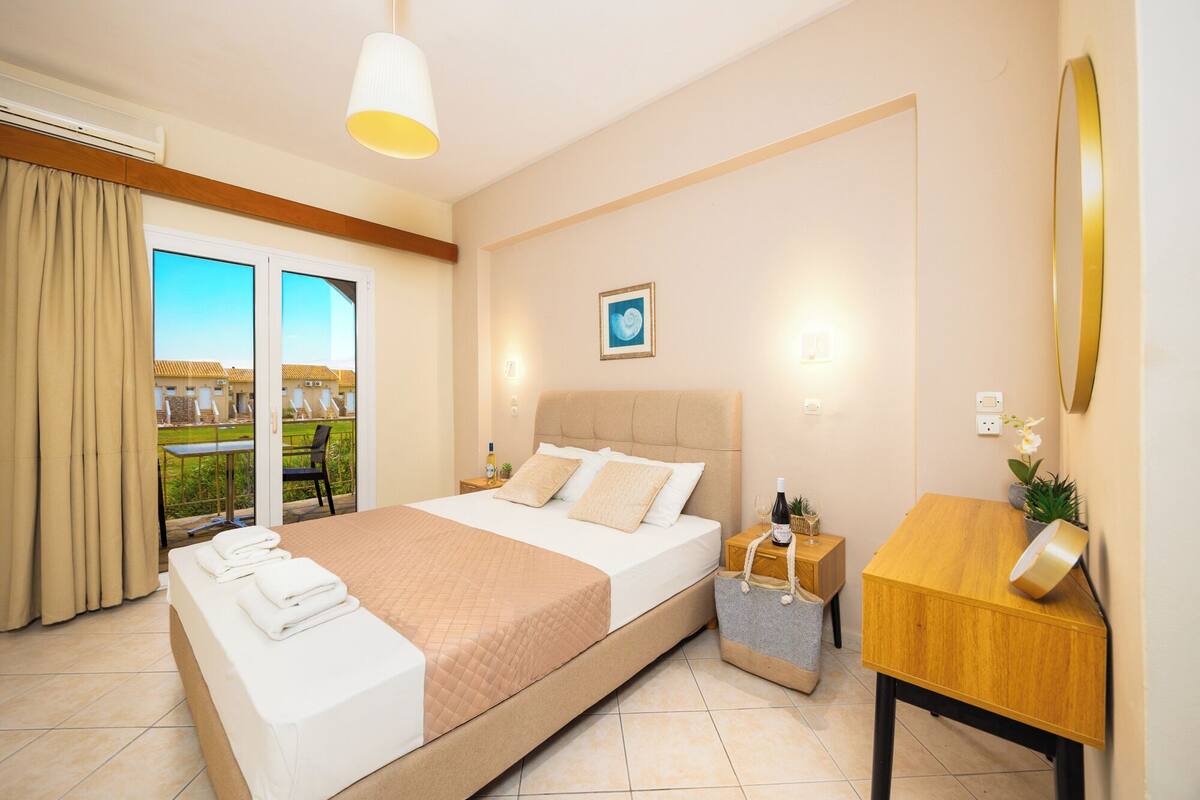 A hotel room with a bed, bedside table, and a view of a pool and building.